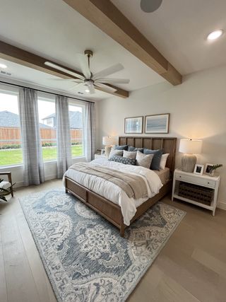 A cozy bedroom featuring wood beams, soft lighting, and a plush patterned rug under the bed.