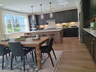 Model Home A modern kitchen with dark cabinetry, a spacious island, and elegant pendant lighting, featuring a cozy dining area with a wooden table.