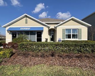 A charming single-story home with a blue awning and manicured shrubs in Buena Lago by D.R. Horton (St. Cloud, FL).