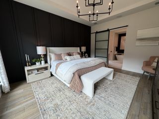 A stylish bedroom featuring a dark accent wall, elegant chandelier, and sliding door leading to a modern bathroom.
