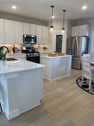 A modern kitchen with white cabinets, stainless appliances, an island, and pendant lighting.
