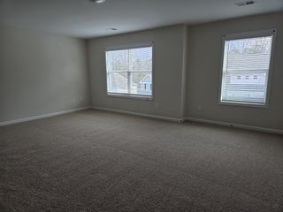 Large carpeted room with multiple windows allowing in natural light, creating a cozy and open atmosphere.