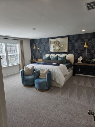 A stylish bedroom featuring a patterned accent wall, plush bedding, and elegant seating for a cozy retreat.