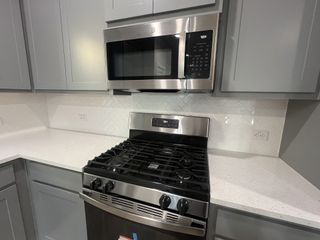 A modern kitchen featuring stainless steel appliances, sleek gray cabinetry, and a white herringbone-tiled backsplash.