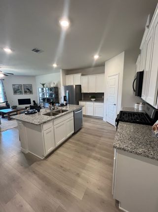 Model Home A modern kitchen with white cabinets, granite countertops, and wood flooring, seamlessly flowing into a cozy living area.