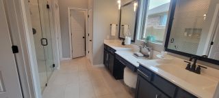 A stylish bathroom with dual vanities, modern fixtures, and a glass-enclosed shower, in a Davis Ranch home by Coventry Homes (San Antonio, TX).