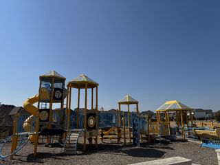 Community Amenities A vibrant playground with yellow and blue structures, slides, and climbing areas, perfect for families in Bluffview by Taylor Morrison (Leander, TX).