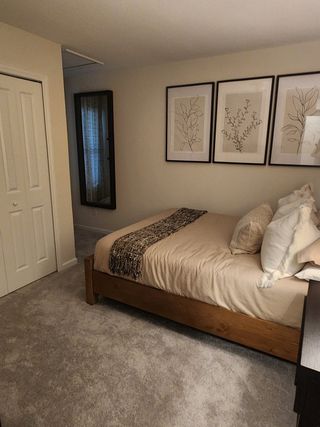 A cozy bedroom features a wooden bed, soft carpet, and framed botanical prints, creating a serene and inviting atmosphere.