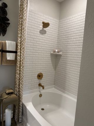 A chic bathroom featuring a white tiled bathtub, brass fixtures, and elegant patterned curtains.