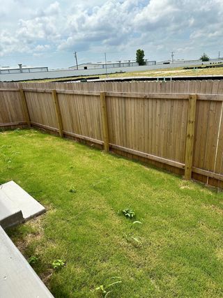 Street view A fenced backyard with lush green grass under a cloudy sky in Wellspring by Clark Wilson Builder (Round Rock, TX).
