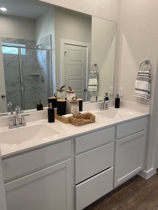 A bright bathroom with a double vanity, modern fixtures, and a marble-tiled shower, in a Hunters Ranch home by View Homes (San Antonio, TX).