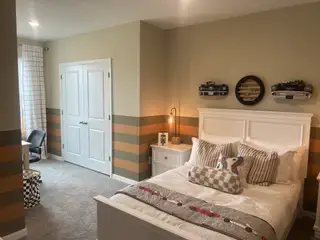 A cozy bedroom featuring striped walls, a white bed, car-themed decor, and a small desk.
