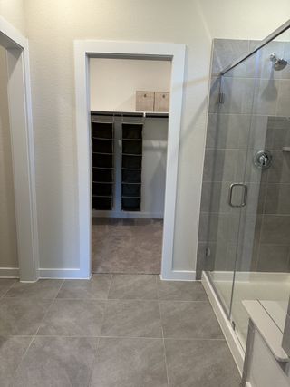 A modern bathroom featuring a glass shower, elegant gray tiles, and direct access to a spacious walk-in closet.
