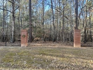 Beautiful wooded entrance to Watkins Glen by Exeter Building Company in Wake Forest, NC, marked by brick pillars and a gate.