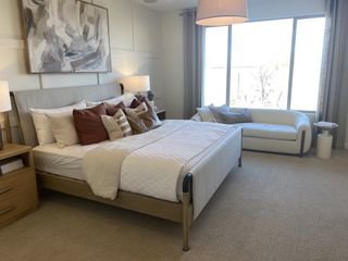 A well-lit bedroom features a textured bed frame, plush bedding, and a cozy sitting area by a large window, creating a serene and inviting space.