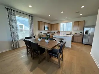 A spacious kitchen with natural wood cabinets, stainless steel appliances, and a large dining table under modern lighting.