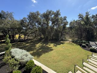 A lush, landscaped backyard with mature trees and manicured shrubs in the Riverstone community by Scott Felder Homes (Georgetown, TX).