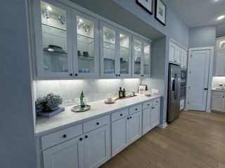 Model Home A charming butler’s pantry with illuminated glass cabinets, white countertops, and modern storage.