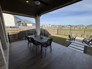 Model Home A cozy patio featuring a stylish dining set, overlooking a fenced backyard with lush green views and a small seating area.