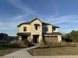 A beautiful stone and stucco home with a manicured lawn in The Colony-Driscoll Bluffs by Sitterle Homes (Bastrop, TX).
