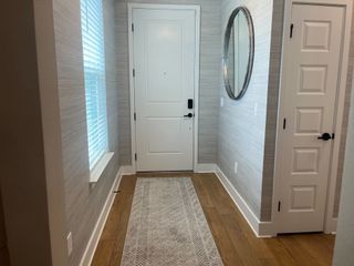 Model Home A welcoming entryway with a white door, textured walls, wood flooring, and a round mirror.