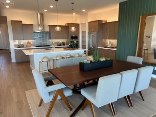 Model Home A modern kitchen with sleek cabinetry, pendant lights, and an elegant dining area featuring a long wooden table and plush chairs.