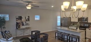 A cozy open-concept living room with plush seating, modern chandelier, and a sleek kitchen featuring a granite island and stainless steel appliances.