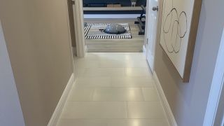 A sleek hallway with light tiles leads to a modern fitness space, featuring an abstract art piece and gym equipment.