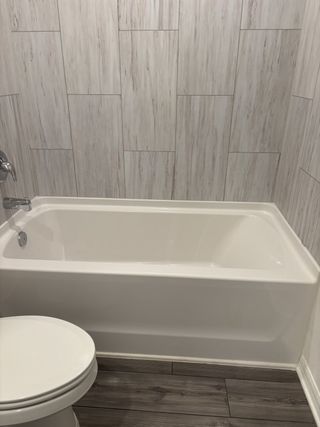 A modern bathroom with sleek wood flooring, a clean white bathtub, and elegant wall tiles.
