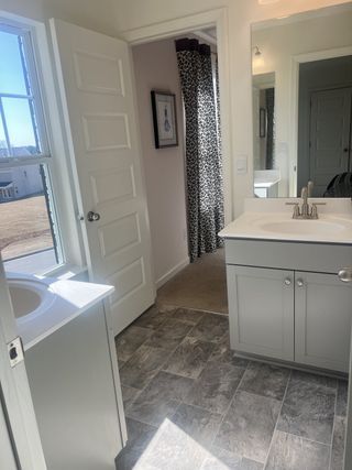 Model Home A bright bathroom with a sleek gray vanity, textured tile flooring, and ample natural light.
