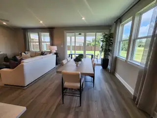 A bright, inviting living area with large windows, comfy seating, and a stylish dining space overlooking a lush backyard.