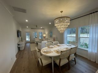 A cozy dining and living area with elegant chandelier, soft lighting, and large windows overlooking serene greenery.