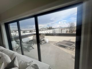 A private balcony extends from a bright living space, featuring outdoor seating and offering panoramic views of the surrounding neighborhood.