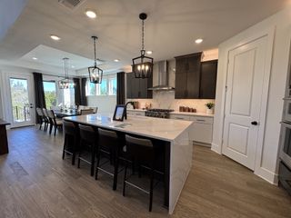 A modern kitchen with a large marble island, sleek dark cabinets, and elegant pendant lighting.