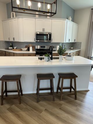 A modern kitchen with white cabinets, a sleek island, and stylish lighting, complemented by wood accents and stools.