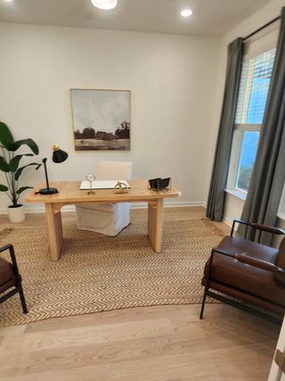 A cozy home office featuring a wooden desk, stylish chairs, modern art, and a large window for natural light.