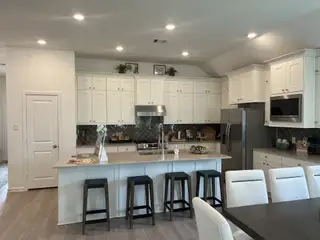 Model Home A modern kitchen with sleek white cabinetry, stainless steel appliances, and a spacious island with bar stools.