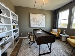 Model Home A contemporary home office with a dark wood desk, abstract art, and cozy yellow chairs, featuring a stylish white bookshelf.