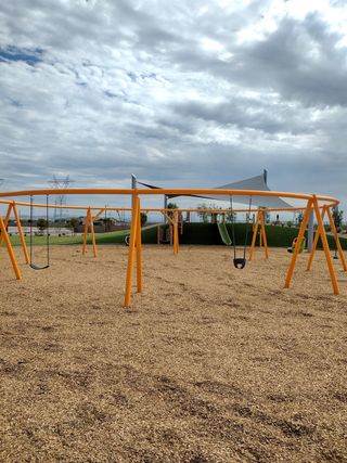 A vibrant playground with orange swings and a shaded pavilion in The Residences Collection at Frontera by New Home Co. (Surprise, AZ).