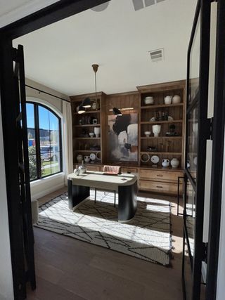 A refined home office with built-in wood shelving, black-framed windows, and contemporary lighting.