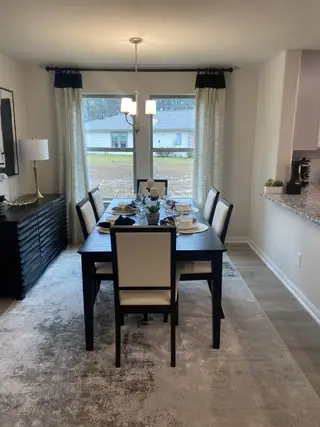 A cozy dining room featuring a dark wood table, elegant chandelier, and natural light streaming through large windows.