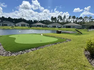 A scenic view of a putting green by a pond in Reverie at Palm Coast by Dream Finders Homes (Palm Coast, FL).