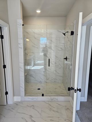 A sleek bathroom featuring a glass-enclosed marble-tiled shower with modern fixtures and natural lighting.
