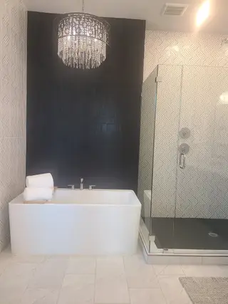 A luxurious bathroom with a sleek bathtub, geometric patterned shower, and elegant chandelier lighting.