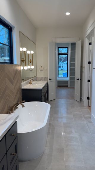 Model Home Bathroom: A luxurious bathroom with a freestanding tub, herringbone tile, dual vanities, and elegant gold fixtures.