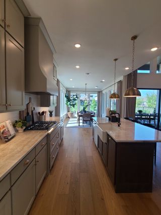 Model Home A spacious kitchen with elegant stone countertops, warm wood flooring, and chic pendant lighting.