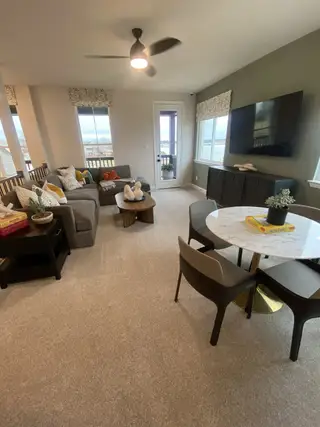 Model Home A cozy living area with a sectional sofa, round coffee table, and TV, featuring a balcony view and modern decor.