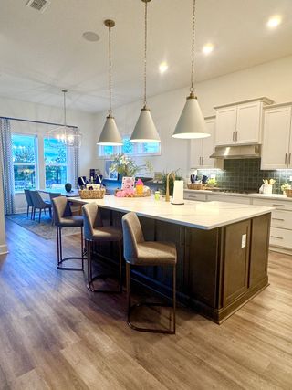 Model Home A modern kitchen with pendant lighting, a large island, and elegant cabinetry, opening to a cozy dining area.