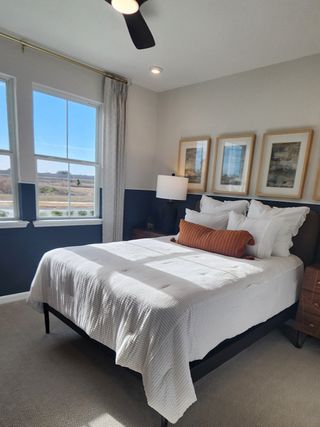 A cozy bedroom featuring a large window, modern fan, and elegant artwork, creating a warm and inviting atmosphere.