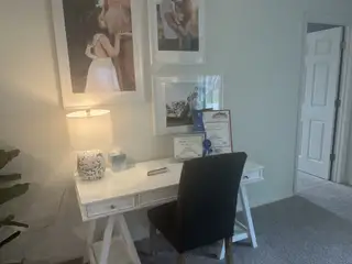 A cozy workspace with a white desk, decorative lamp, framed photos, and awards, creating an inspiring home office.